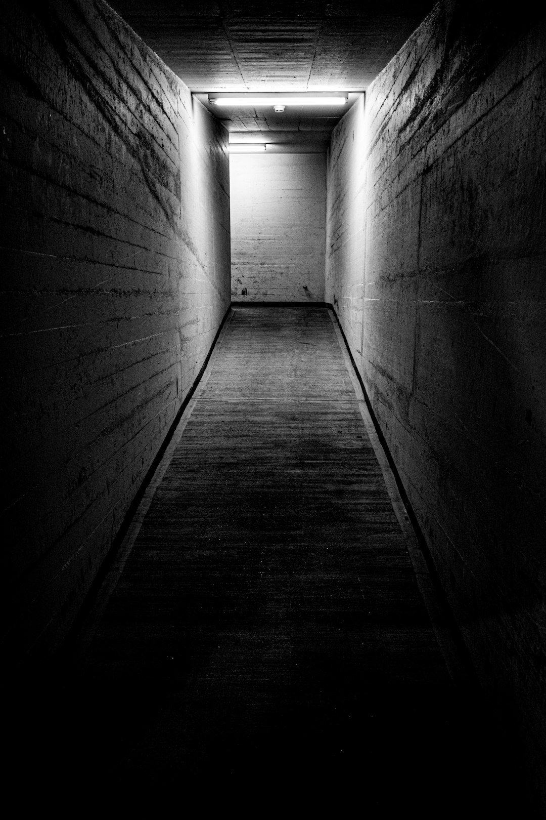 Cold War passage inside the Sonnenberg bunker in Lucerne, Switzerland. Black and white photo of a narrow concrete corridor with stark lighting, symbolizing isolation, secrecy and the hidden scale of underground civil defense shelters.