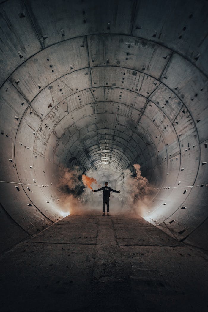 A person stands in a dramatic, smoky metal tunnel, creating a mysterious atmosphere.