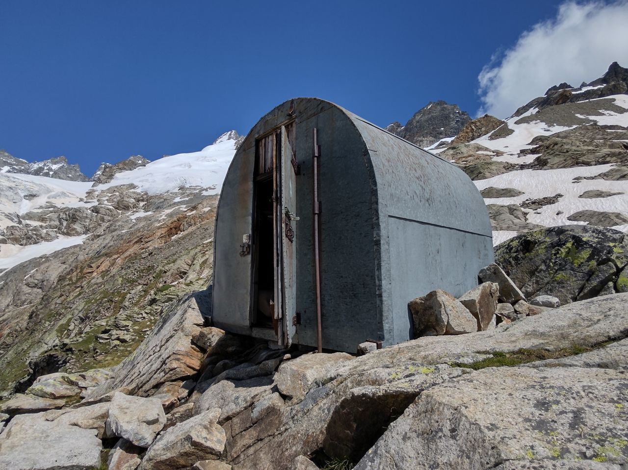 A solitary mountain shelter nestled among rocks with a clear blue sky and snowy peaks in Orsières, Switzerland.