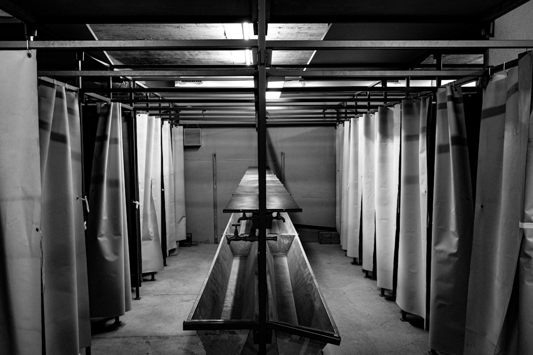 Cold War washing facilities inside the Sonnenberg bunker in Lucerne, Switzerland. Black and white photo of communal wash basins and shower stalls with curtains, reflecting the stark functionality of underground civil defense shelters.